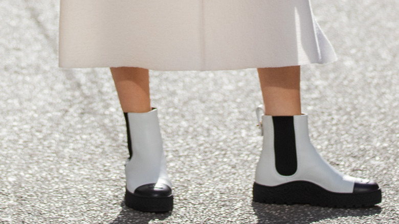 A person wears white Chelsea boots and a white skirt