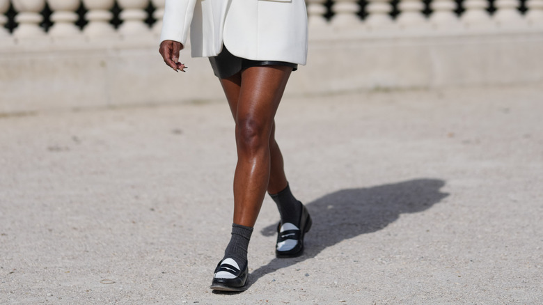 A person in a skirt wearing black and white loafers with socks