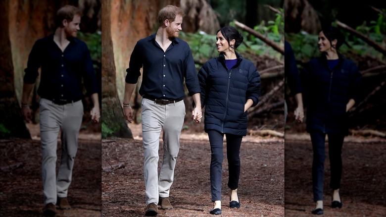 Prince Harry and Meghan Markle smiling at each other while walking outside in the woods.
