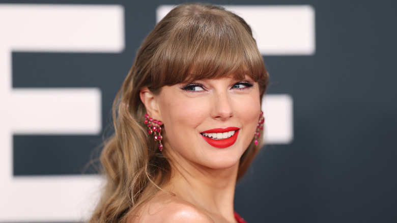 Taylor Swift on a red carpet with a red lip and red earrings