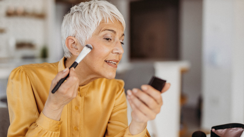 Woman with white hair applying makeup