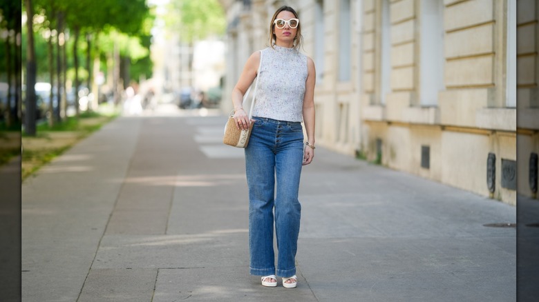 A woman wearing bootcut jeans styled with a knit top, sunglasses, and platform white sandals