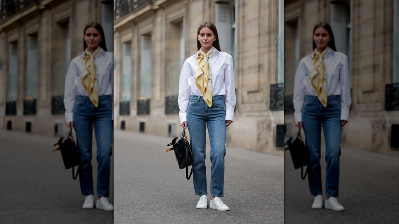 A person wearing straighty-leg medium-wash jeans with white sleek sneakers