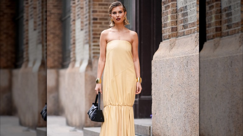 A woman wearing a yellow draped dress with a black handbag