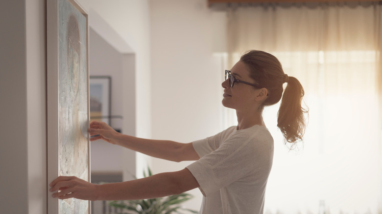 woman hangs up painting on wall