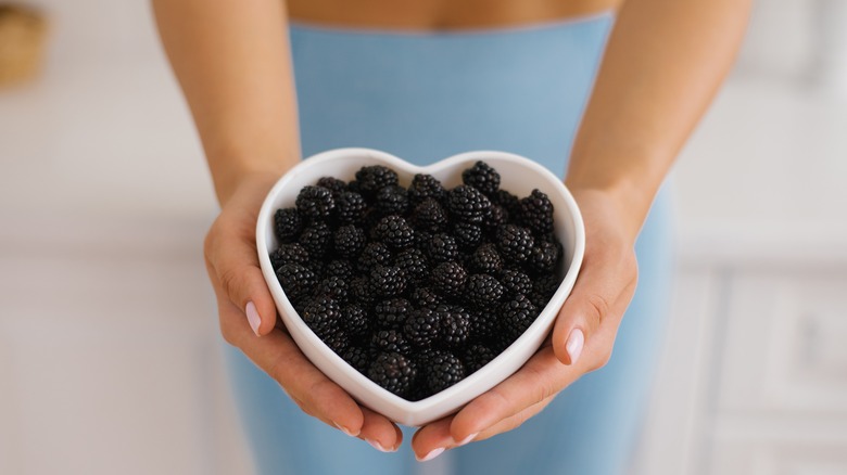 Closeup of woman holding fresh blackberries in white bowl