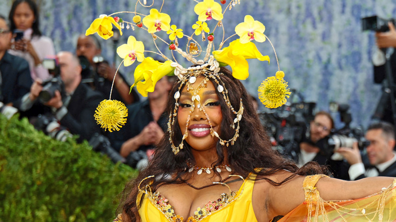 SZA posing at the 2026 Met Gala wearing an ornate yellow flower headdress.