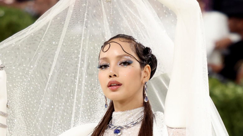 Blackpink's Lisa posing at the 2026 Met Gala in a white gown with part of it flowing behind her face.