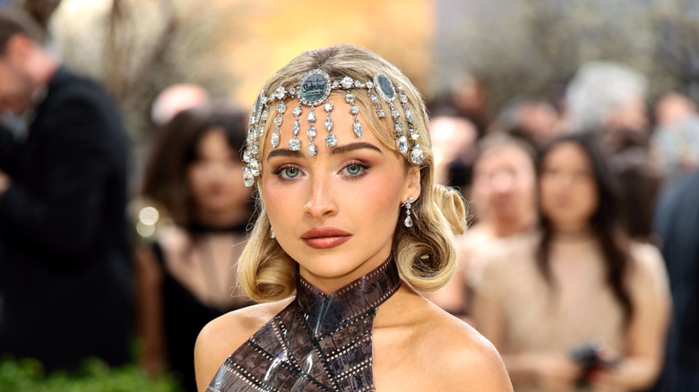 Sabrina Carpenter posing at the 2026 Met Gala with an ornate headdress and a film-strip halter top.