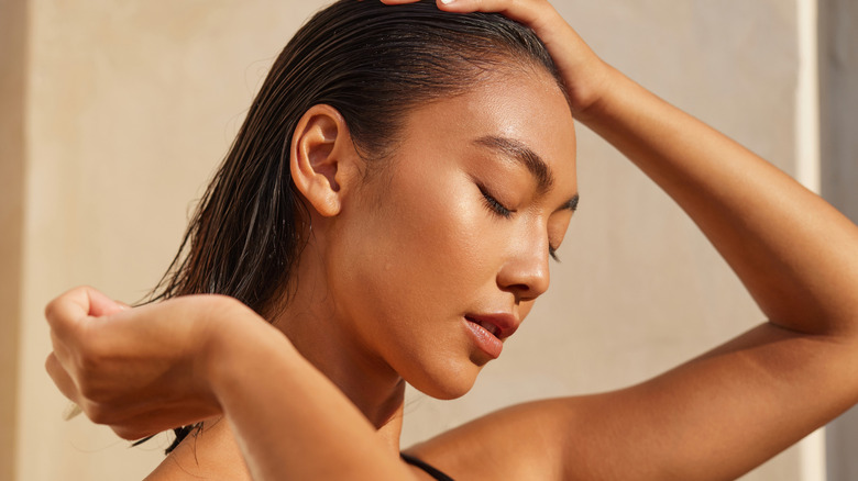 A woman with dewy, radiant skin touching her head