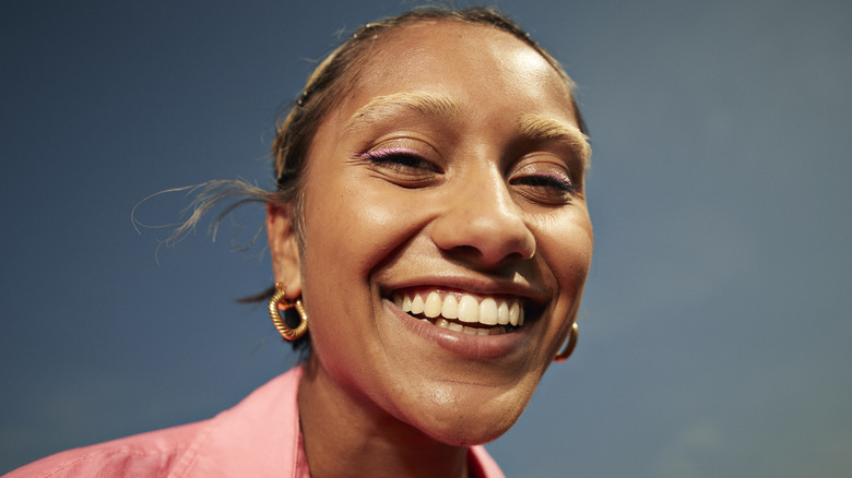A person with an oval face wearing geometric gold earrings
