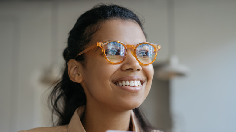 A person with warm skin and tortoiseshell glasses smiling