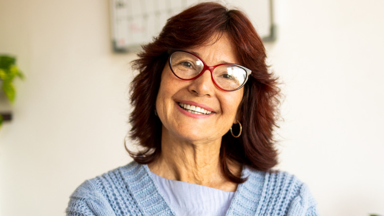 An odler woman with an auburn shag and glasses smiles