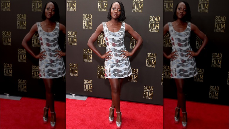 Lupita Nyongo posing on a red carpet in a silver minidress.