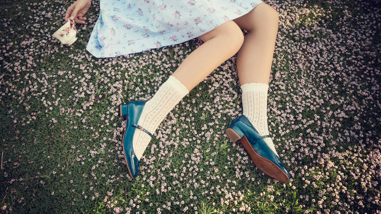 A young woman sitting on a garden wears blue Mary Jane shoes worn with lace mid calf socks