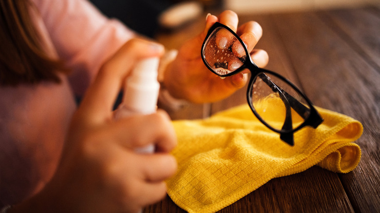 A woman cleans her eye glasses with a lens spray and microfiber cloth