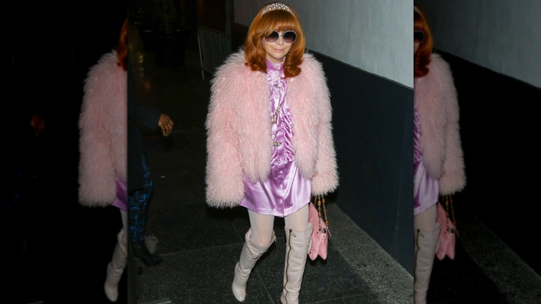 A woman walking with red hair, an embellished headband, and a pink fluffy jacket