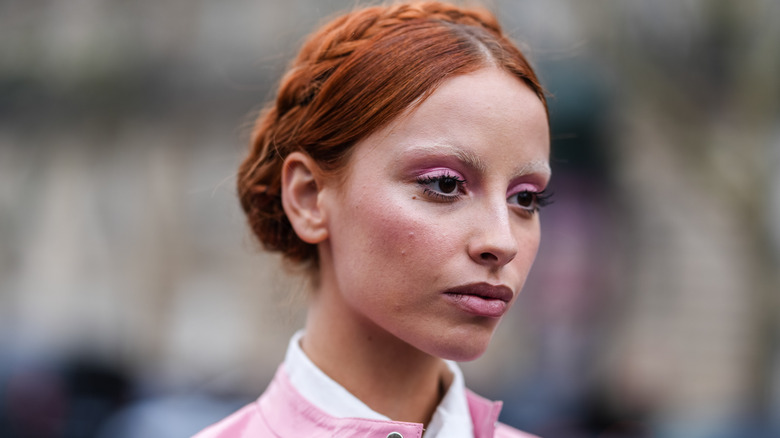 A woman with orange braided hair wearing a pink jacket