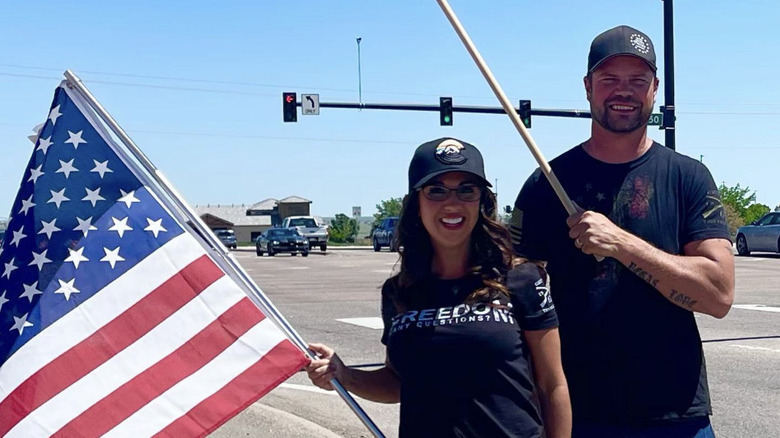 Lauren Boebert and her exhusband Jayson Boebert stand on the side of the road waving American flags