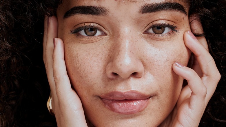 Woman with freckles touching face