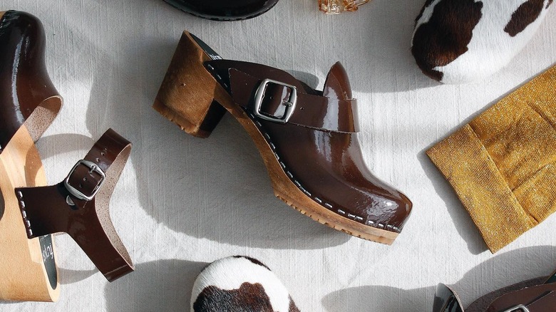 brown blogs and cow print clogs laying against a gray background