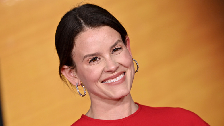 Sosie Bacon smiles for cameras while wearing a red dress