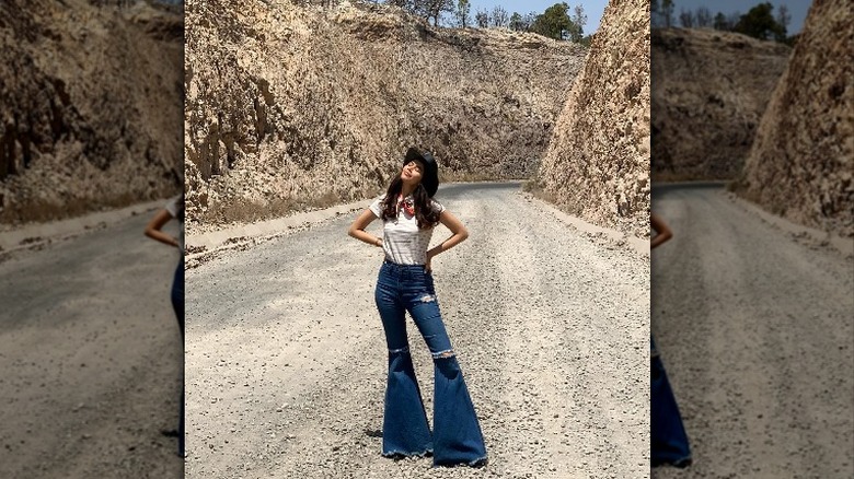 woman standing in a dirt road wearing a striped tee shirt, neck scarf, and high rise ultra flare jeans
