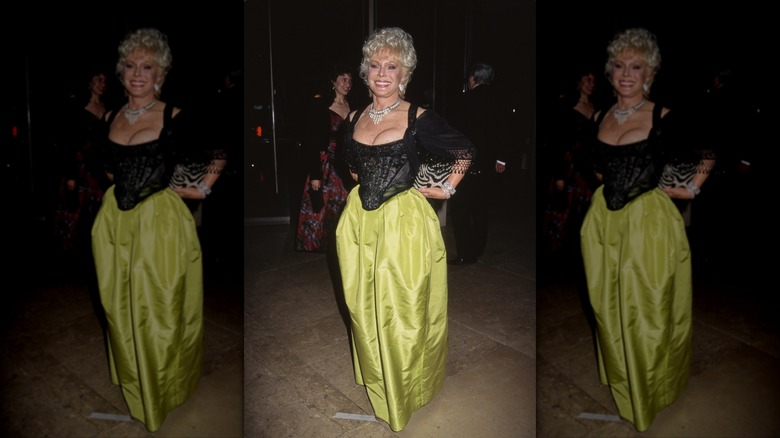 Eva Gabor smiles wearing a black corset, green skirt, and statement necklace.