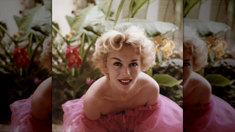 Eva Gabor smiles wearing red lipstick and a pink tulle dress.