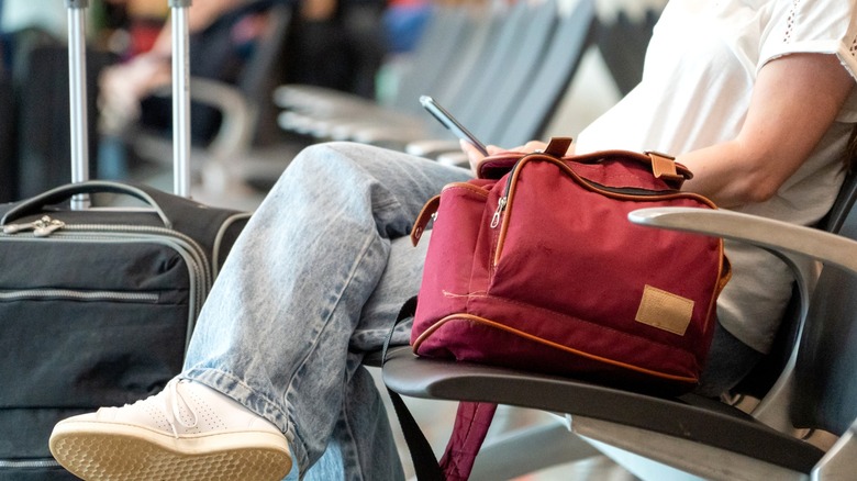 A woman sitting an an airport gate in jeans and a white T-shirt.