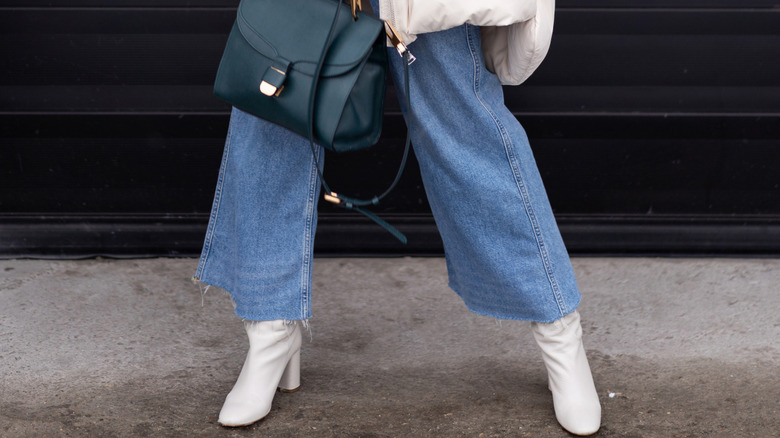 A woman wearing cropped flare jeans, boots, and a black bag