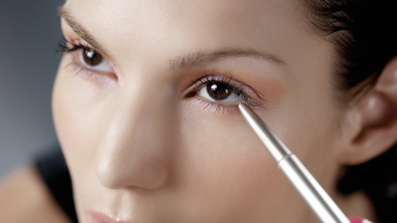 woman looking up applying eyeliner