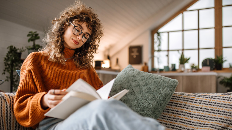 A person with glasses reading a book on the couch
