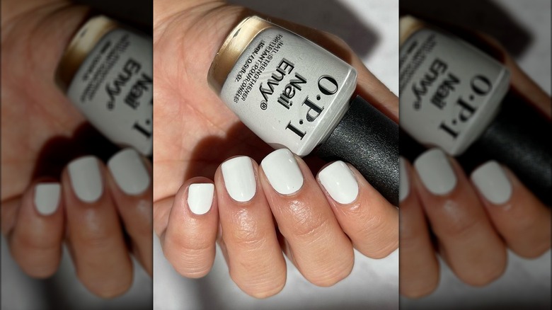 Hand with white painted nails holding a bottle of polish