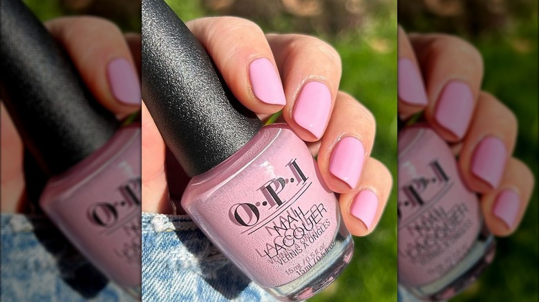 Manicured hand holding a pale pink bottle of nail polish