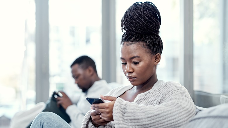Two people using phones on sofa
