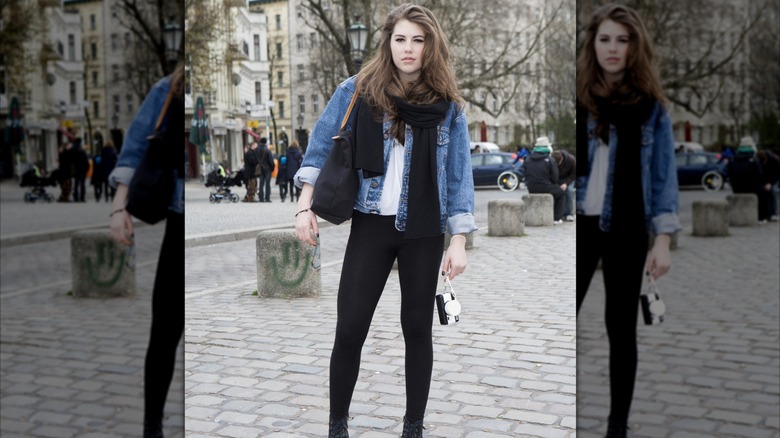 A woman wearing leggings, boots, a white shirt, and a jean jacket posing for a picture