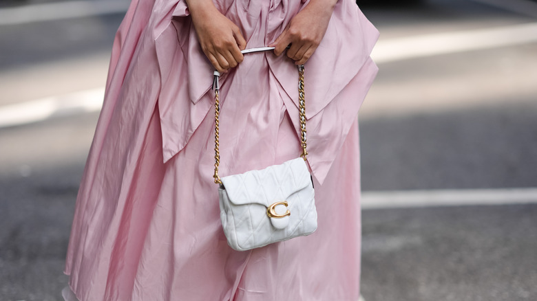 A person holding a white Coach bag with gold hardware and a C logo