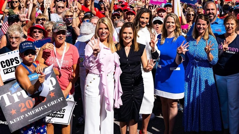 Pam Bondi wearing a pink ruffle top and white pants at a rally