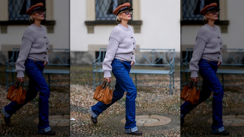 A perso wearing straight cuffed jeans and a chunky boots with a cardigan and baker's hat