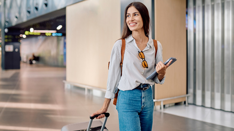 A woman wearing jeans while pulling a suitcase at an airport