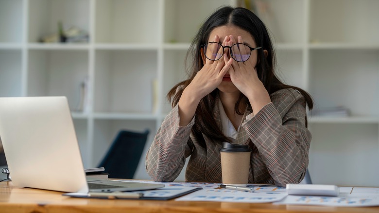 Woman rubs her eyes at her work desk