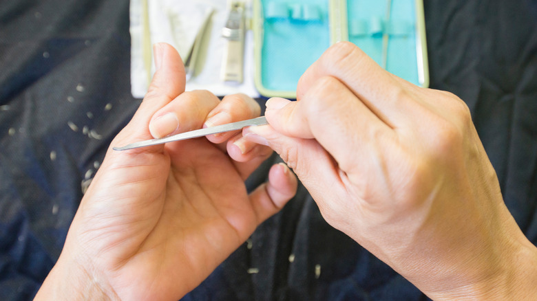 A person filing their own nails with a kit in the background