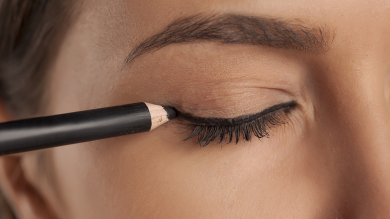 woman applying black pencil eyeliner