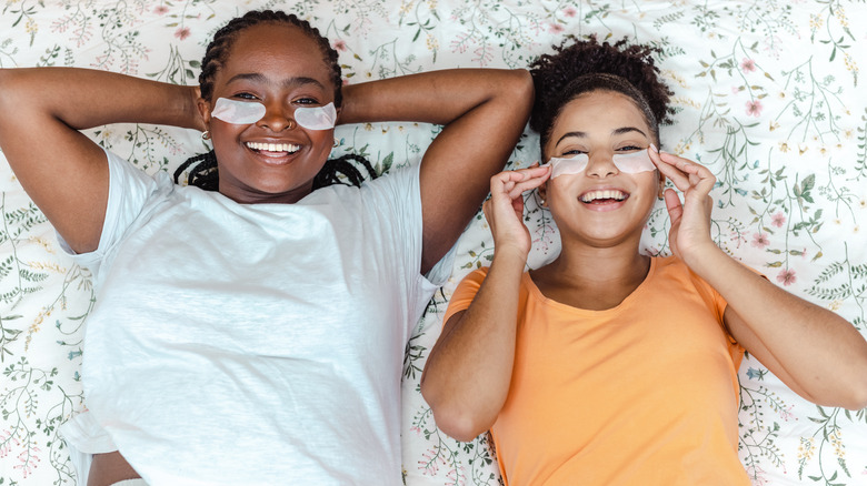 Two women on bed wearing skincare treatment pads