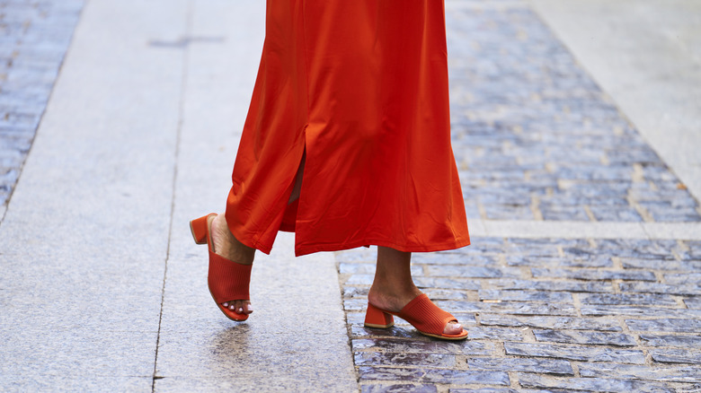 Someone walking in orange peep-toe mules worn with an orange skirt