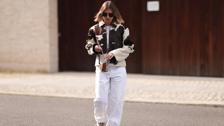 A person wearing baggy white jeans, sunglasses, and a cow-print top