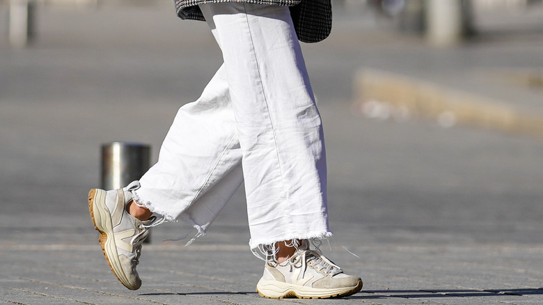 A person wearing beige and white sneakers with white baggy jeans