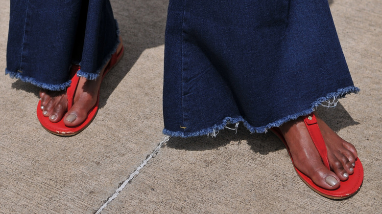 A woman wearing bell bottoms and red sandals with muted nail polish