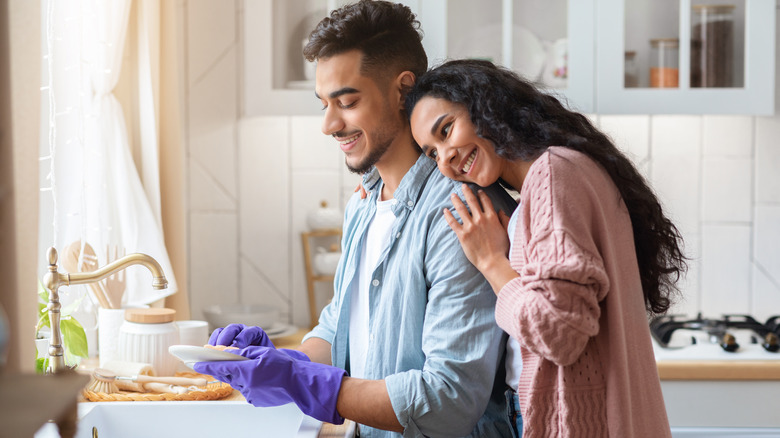 woman leaning over a man washing dishes